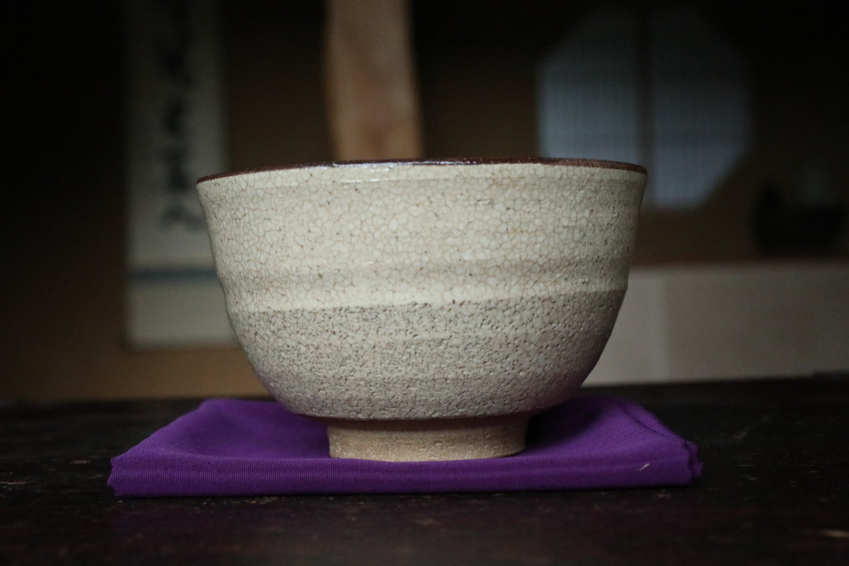 A white ceramic bowl with a speckled texture sits on a purple cloth on a dark wooden surface.