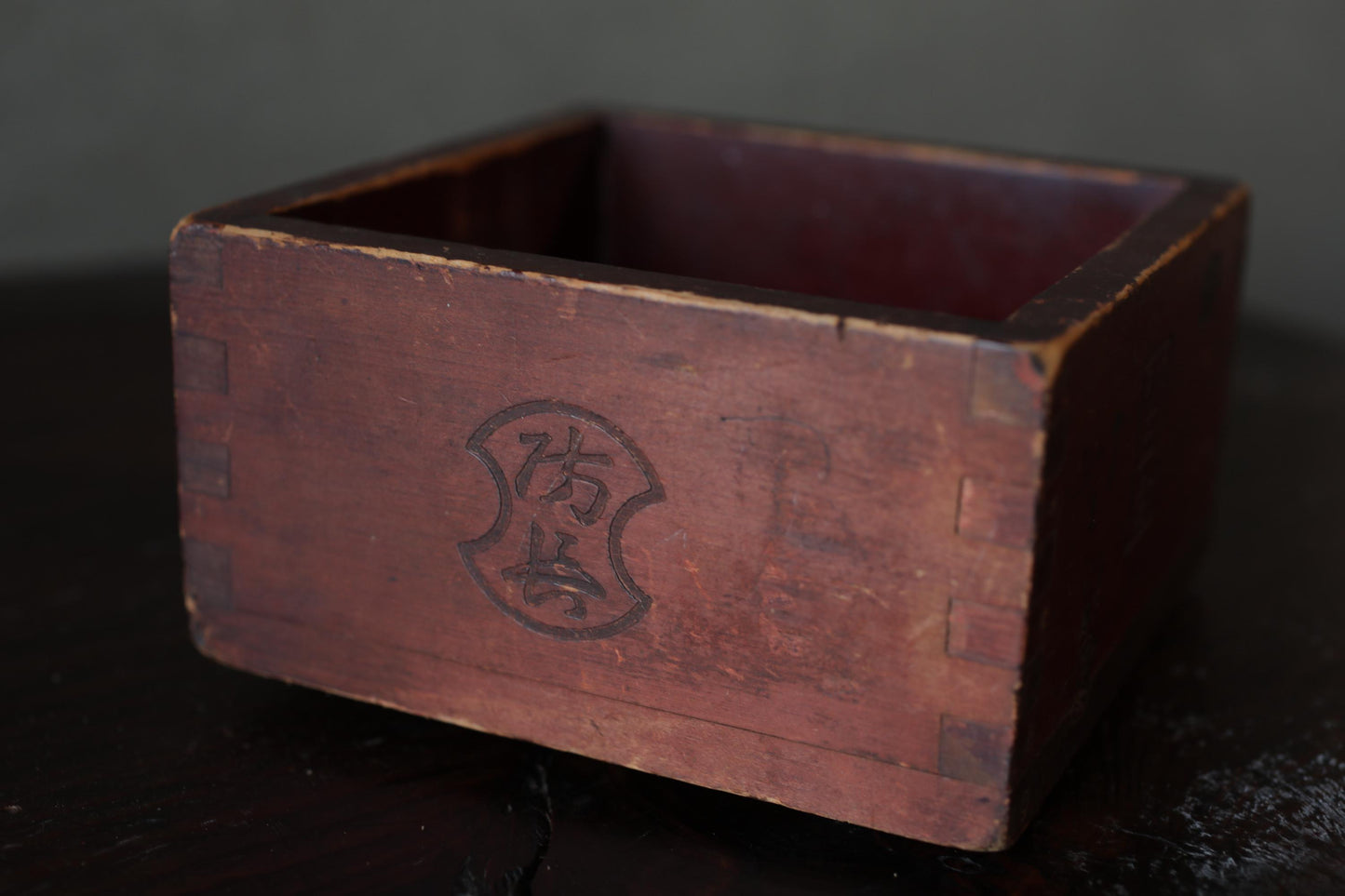 An old, weathered wooden box with a carved design on its side, sitting on a dark surface.