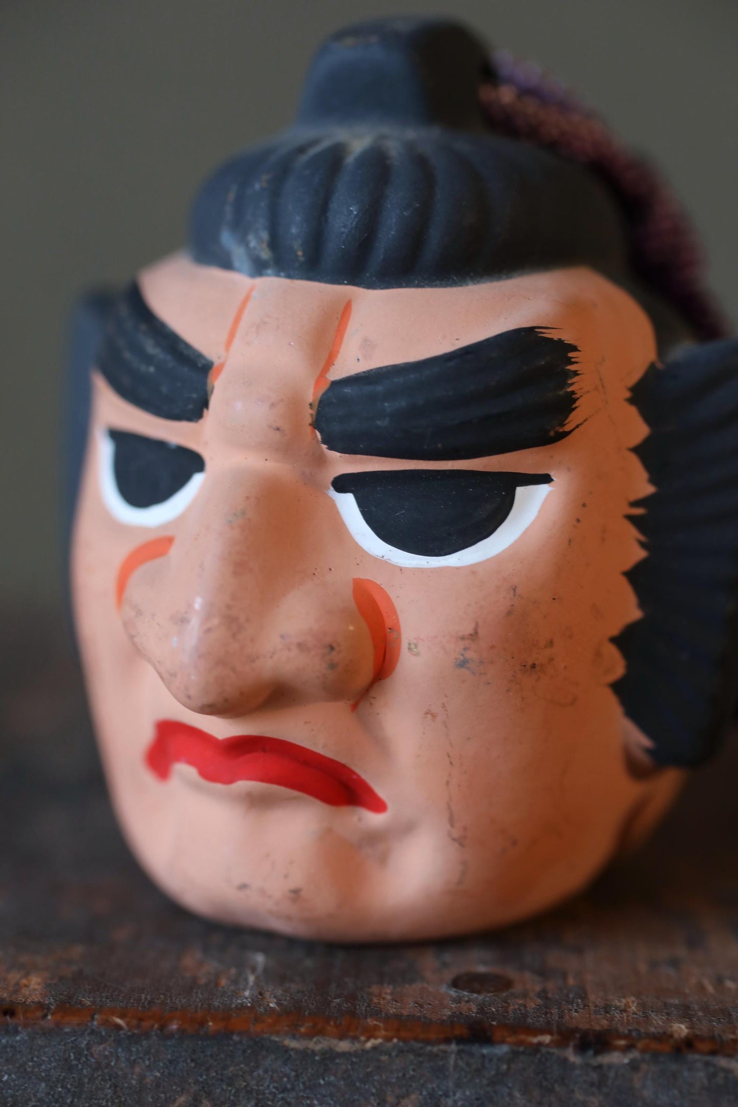 A close-up image of a ceramic mug or container with a face painted on it, featuring a red mouth and black features.