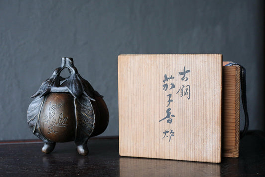 a small bronze figurine of an apple with leaves, placed next to a wooden box with Japanese characters on it.