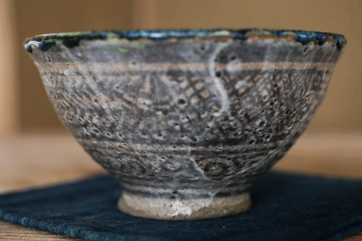 A close-up image of a ceramic bowl with a detailed pattern on its surface, placed on a dark cloth.