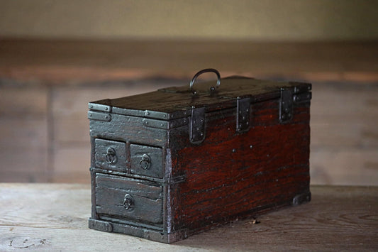 An old, wooden chest with metal clasps sits on a wooden surface.
