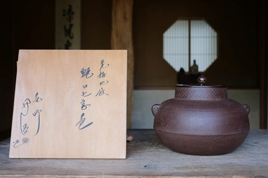a wooden sign with Japanese characters next to a large brown ceramic pot on a wooden surface.