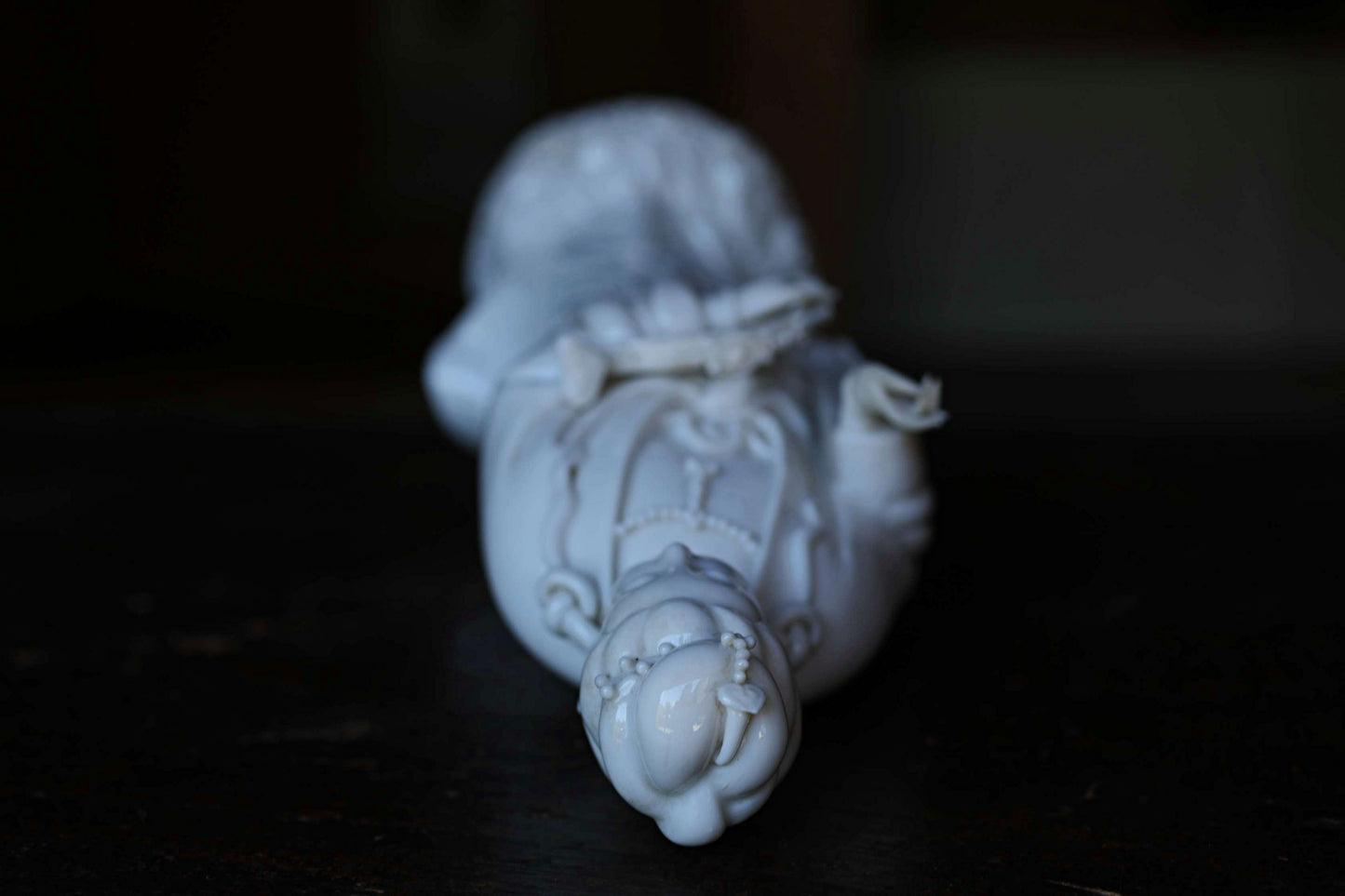A white porcelain figurine of a person lying down on a dark surface.