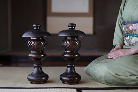 A person in a green kimono is seated on the floor, with two ornate lanterns placed next to them.