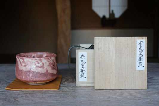 a wooden box with Japanese text on it, placed on a wooden table, alongside a pink ceramic bowl.