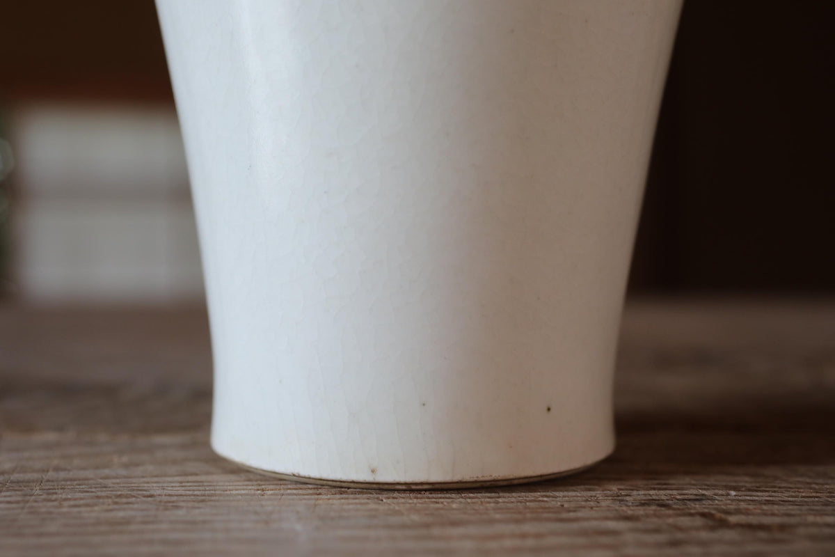 A white ceramic cup or vase placed on a wooden surface.