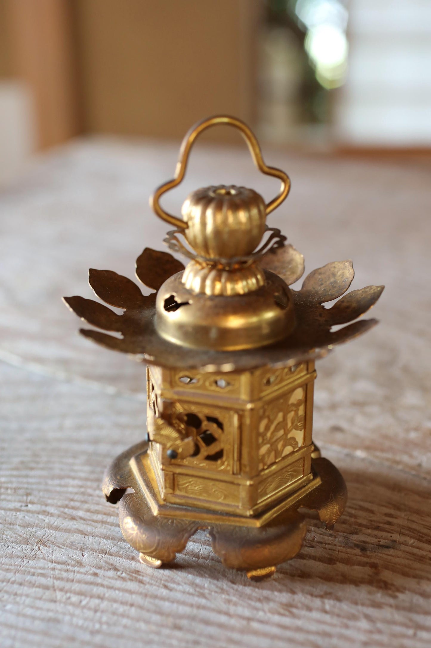 A small, ornate brass lantern with a decorative top sits on a wooden surface.