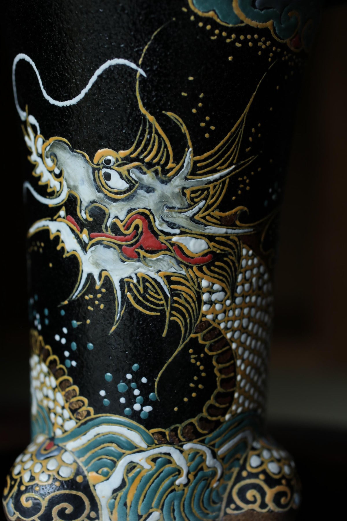 a close-up view of a decorative vase with a dragon design on it. The vase is black and has a detailed, intricate pattern with gold and white accents.