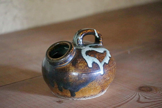 A ceramic pitcher with a handle and spout sits on a wooden surface.