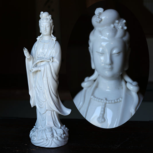 two white ceramic statues of female deities, one standing upright and the other in profile view.