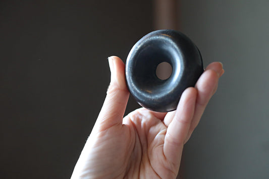 A hand holding a black object with a hole in the center, against a dark background.