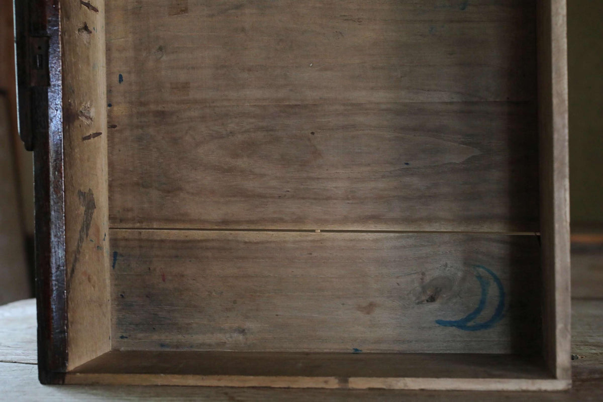 an empty wooden box with a blue drawing of a crescent moon on the bottom right corner.
