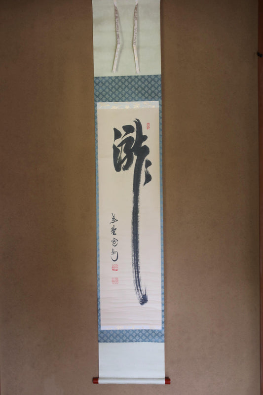 a vertical banner with a calligraphy design and some text. The banner is hanging on a wall and appears to be a scroll or a banner.