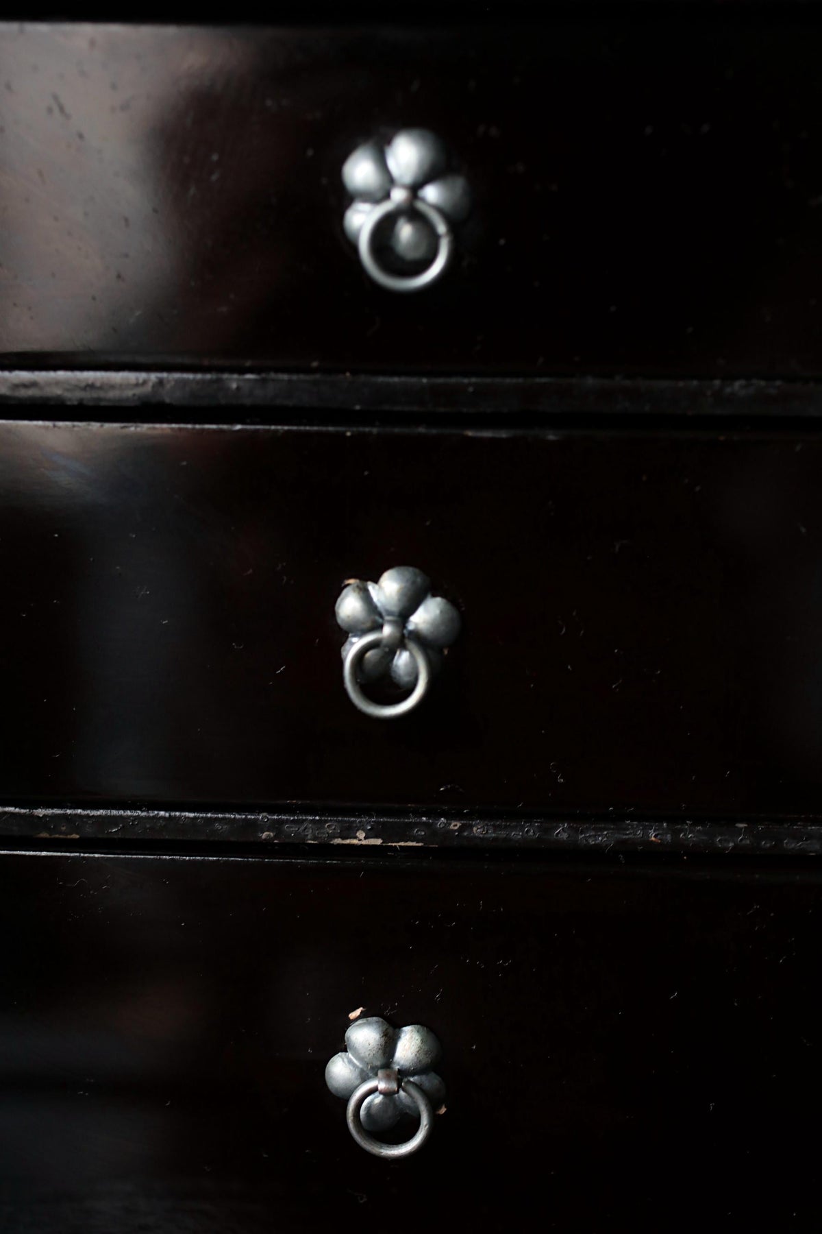 a close-up view of a dark wooden drawer with three metal handles, each with a flower-shaped design.