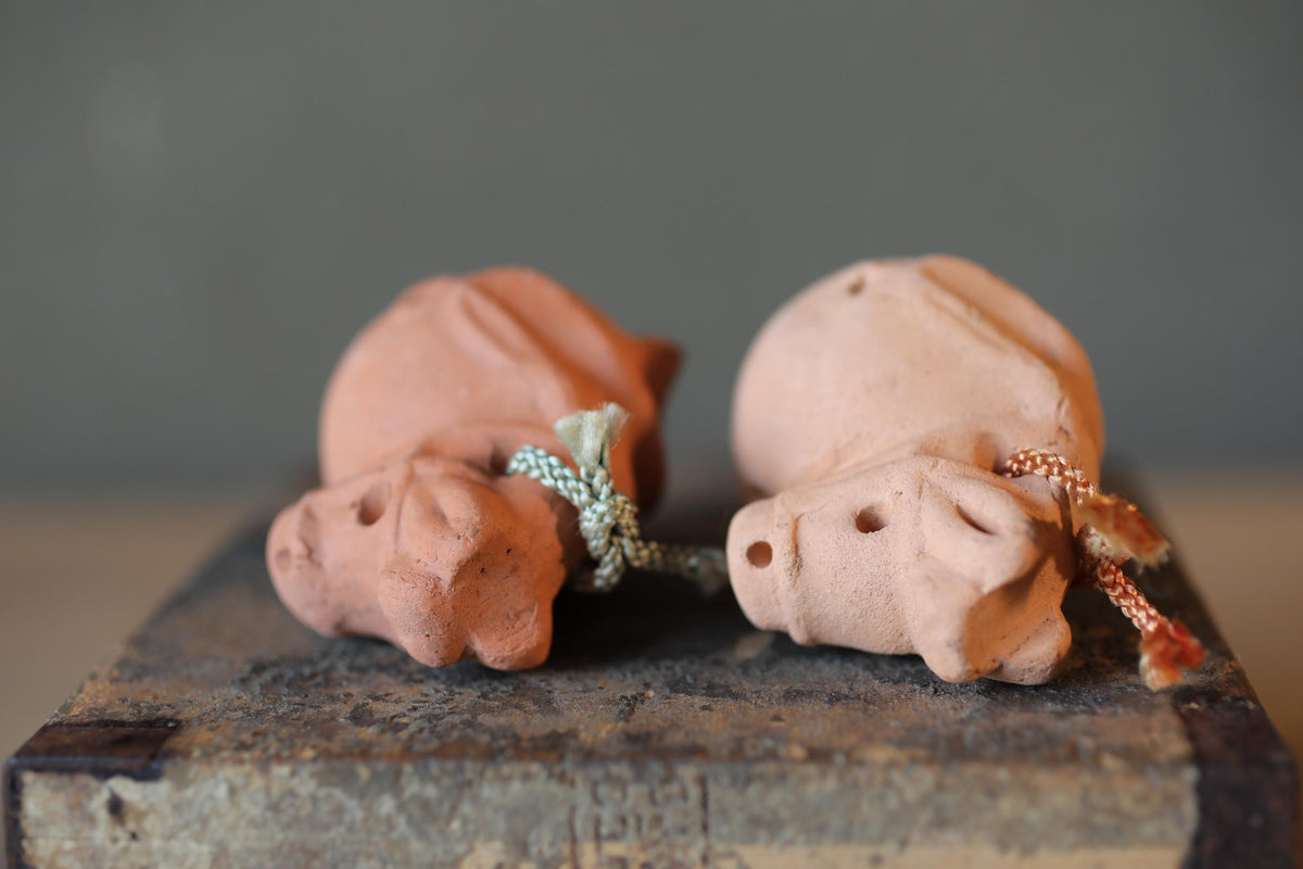 Two small clay figurines of pigs, one pink and one brown, are sitting on a wooden surface.