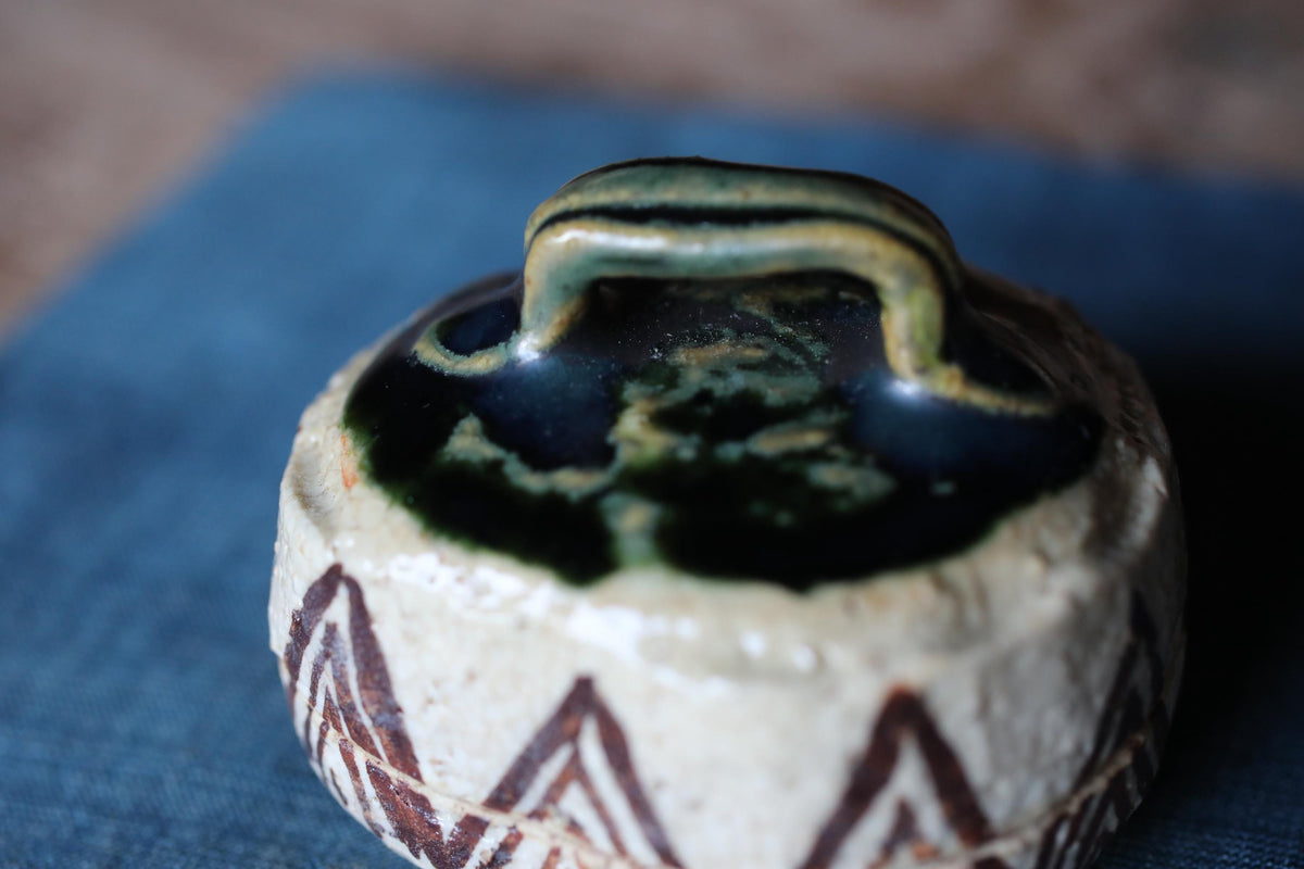 A close-up image of a ceramic container with a handle, featuring a patterned design on its surface.