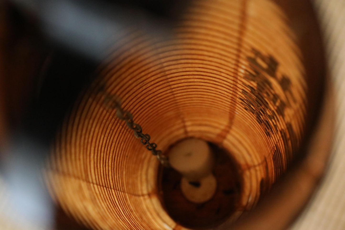 a close-up view of a wooden object, possibly a piece of furniture or a decorative item, with a spiral pattern and a chain visible inside the object.