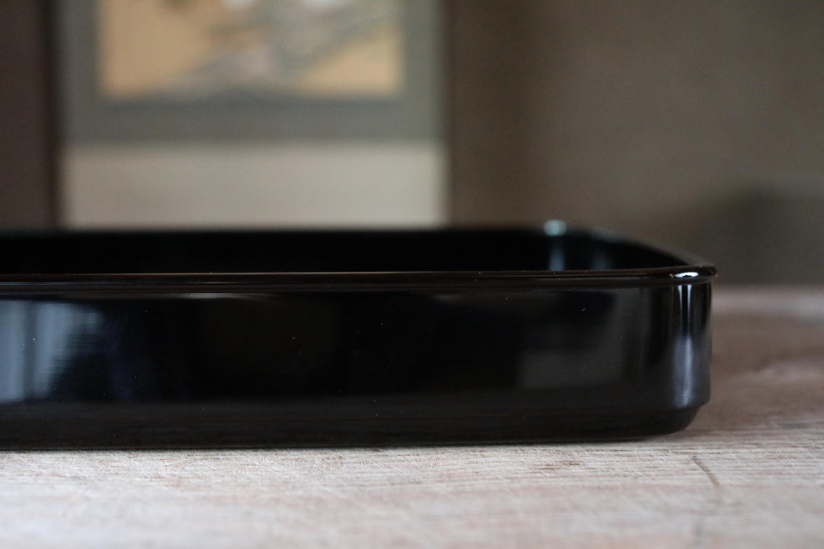 A black rectangular baking dish sits on a wooden surface, with a blurred background.