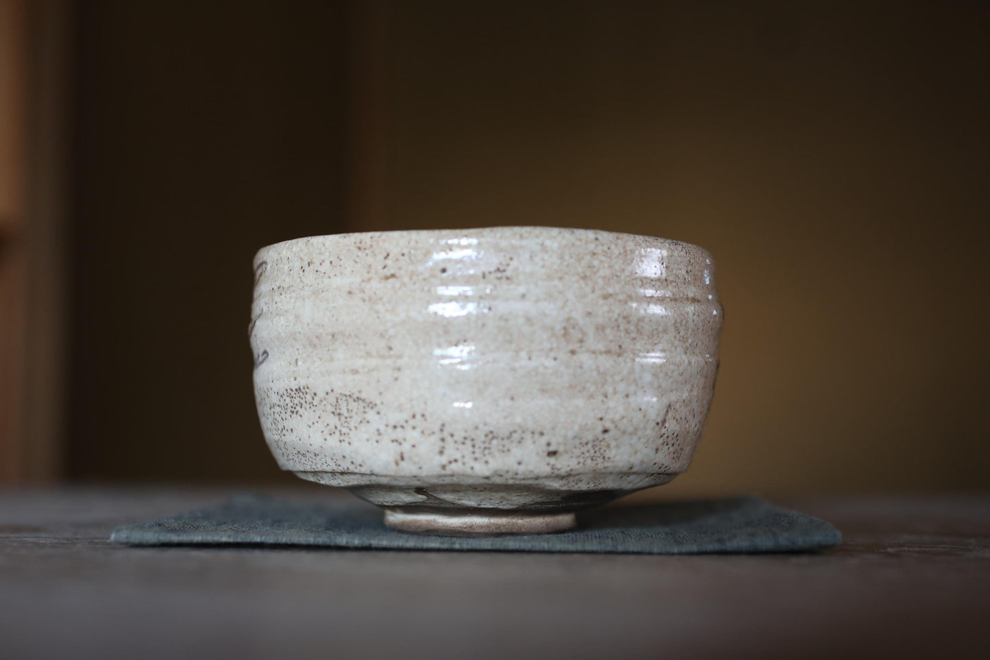 A white ceramic bowl with a textured surface sits on a dark cloth on a wooden surface.