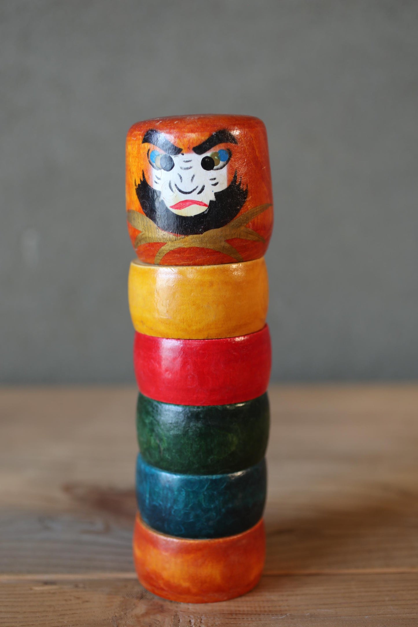 A colorful wooden toy with a painted face and a row of rings on top, sitting on a wooden surface.