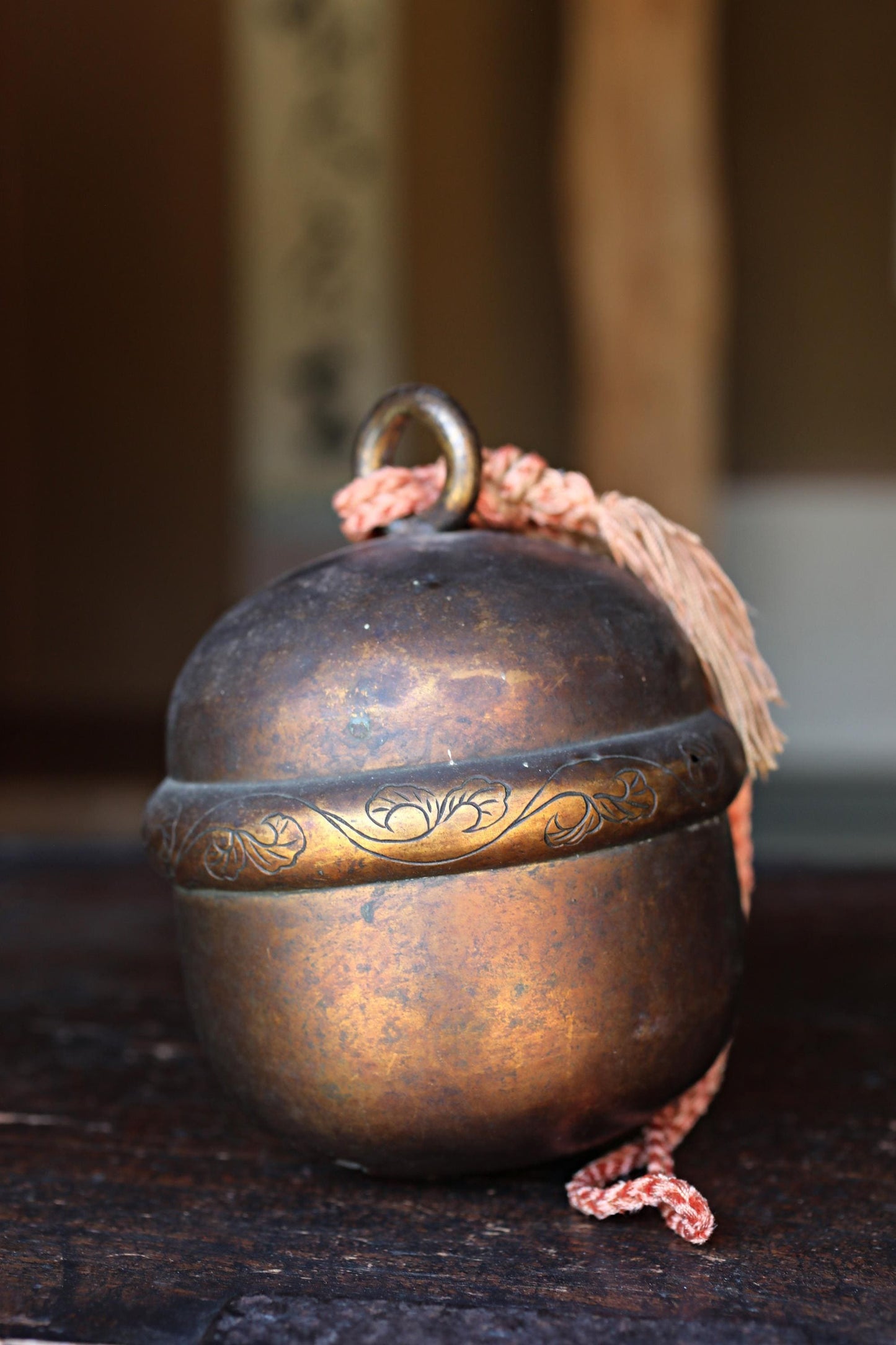 An old, rusted metal bell with a decorative band around it, sitting on a wooden surface.