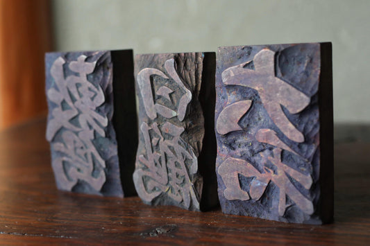Three dark rectangular blocks with intricate carved designs on their surfaces, placed on a wooden surface.