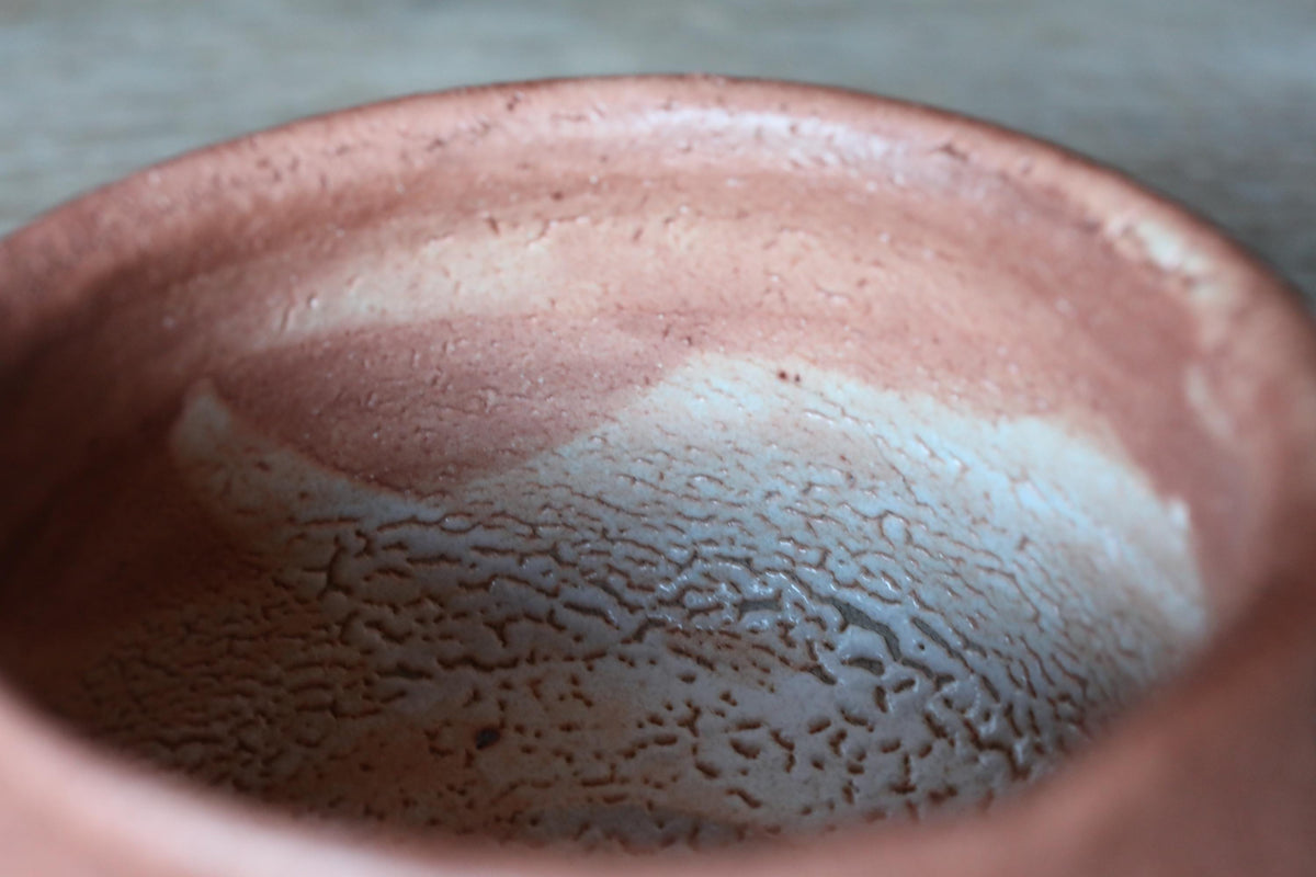 A close-up image of a ceramic bowl with a textured surface, featuring a pinkish-brown hue and a white speckled pattern.