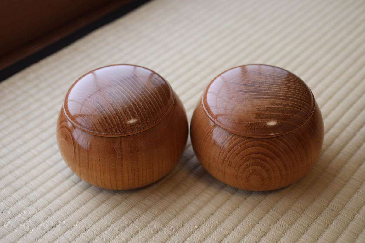 Two wooden bowls with lids sit on a woven mat.