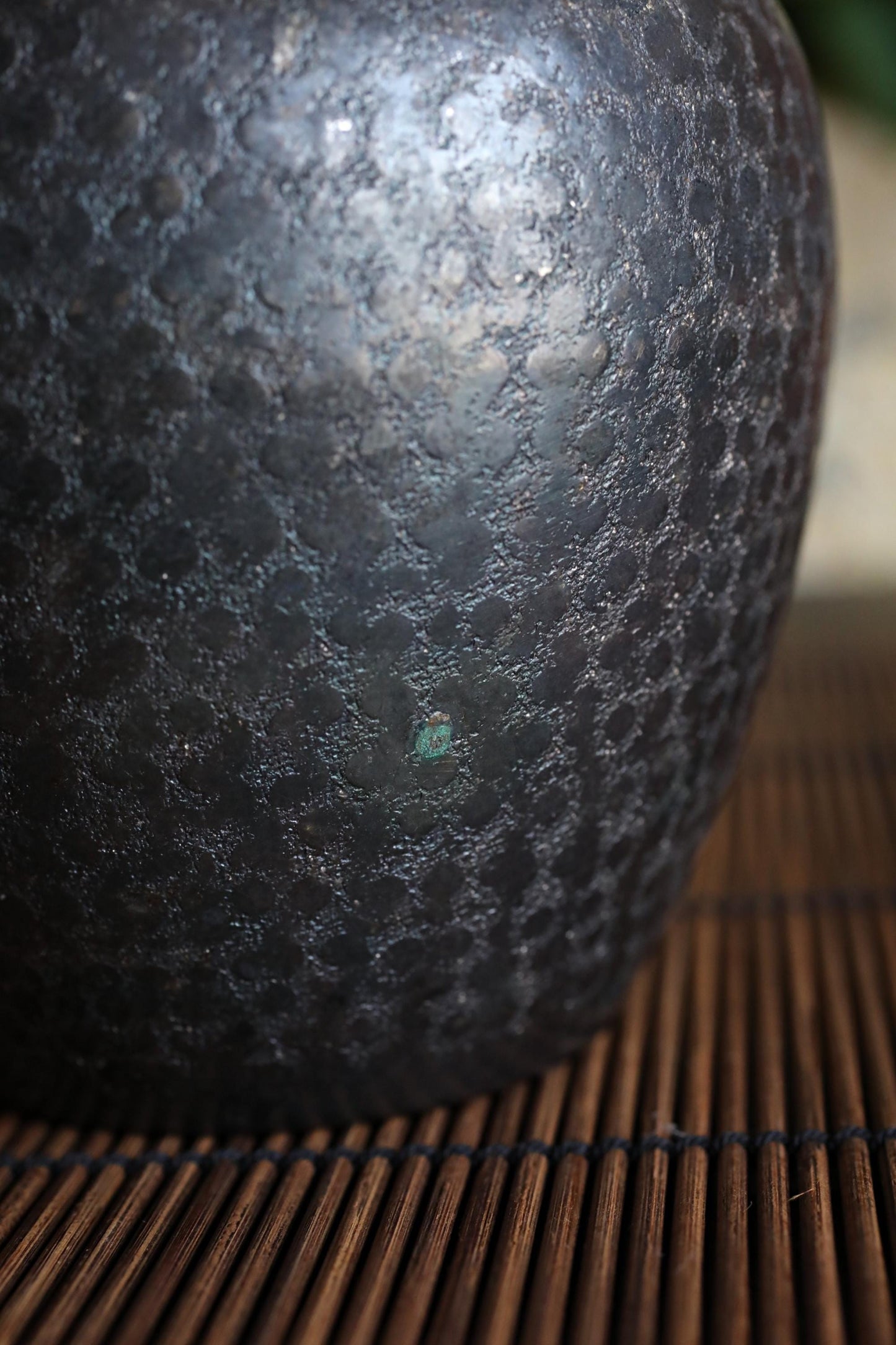 A close-up view of a textured, dark-colored vase or container with a metallic, speckled surface.