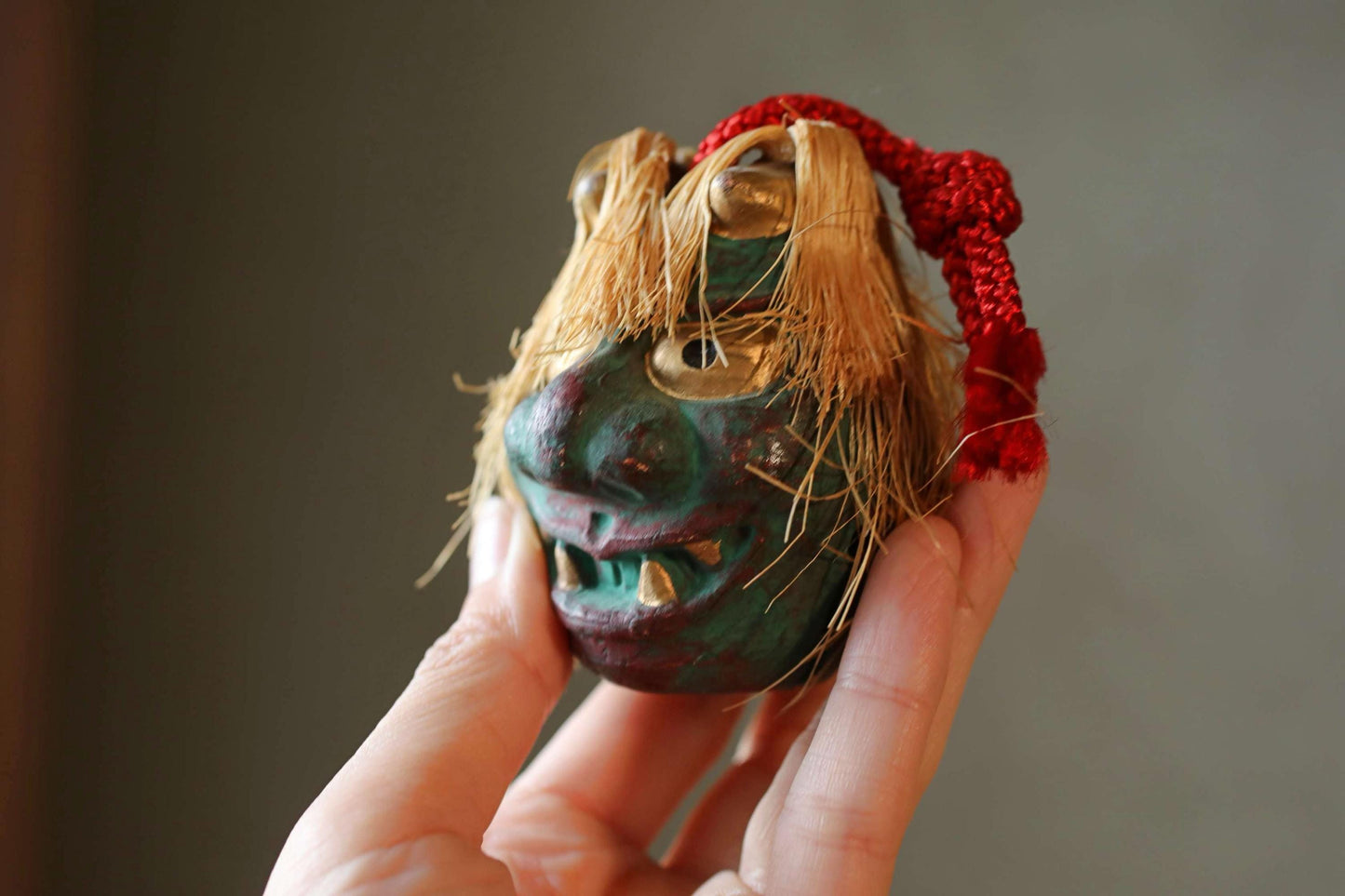 A hand holding a small, colorful mask with a red string around it.