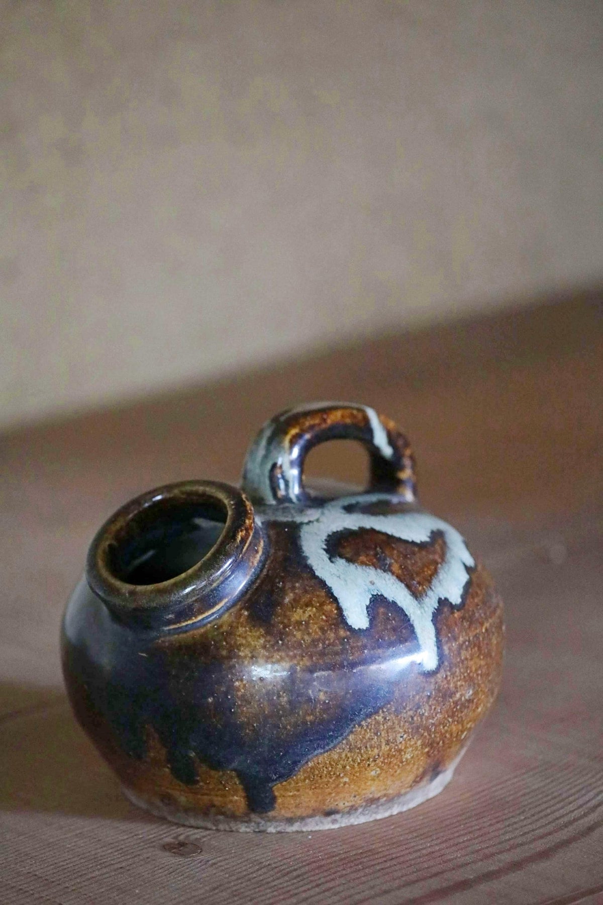 A ceramic pitcher with a handle and spout sits on a wooden surface.