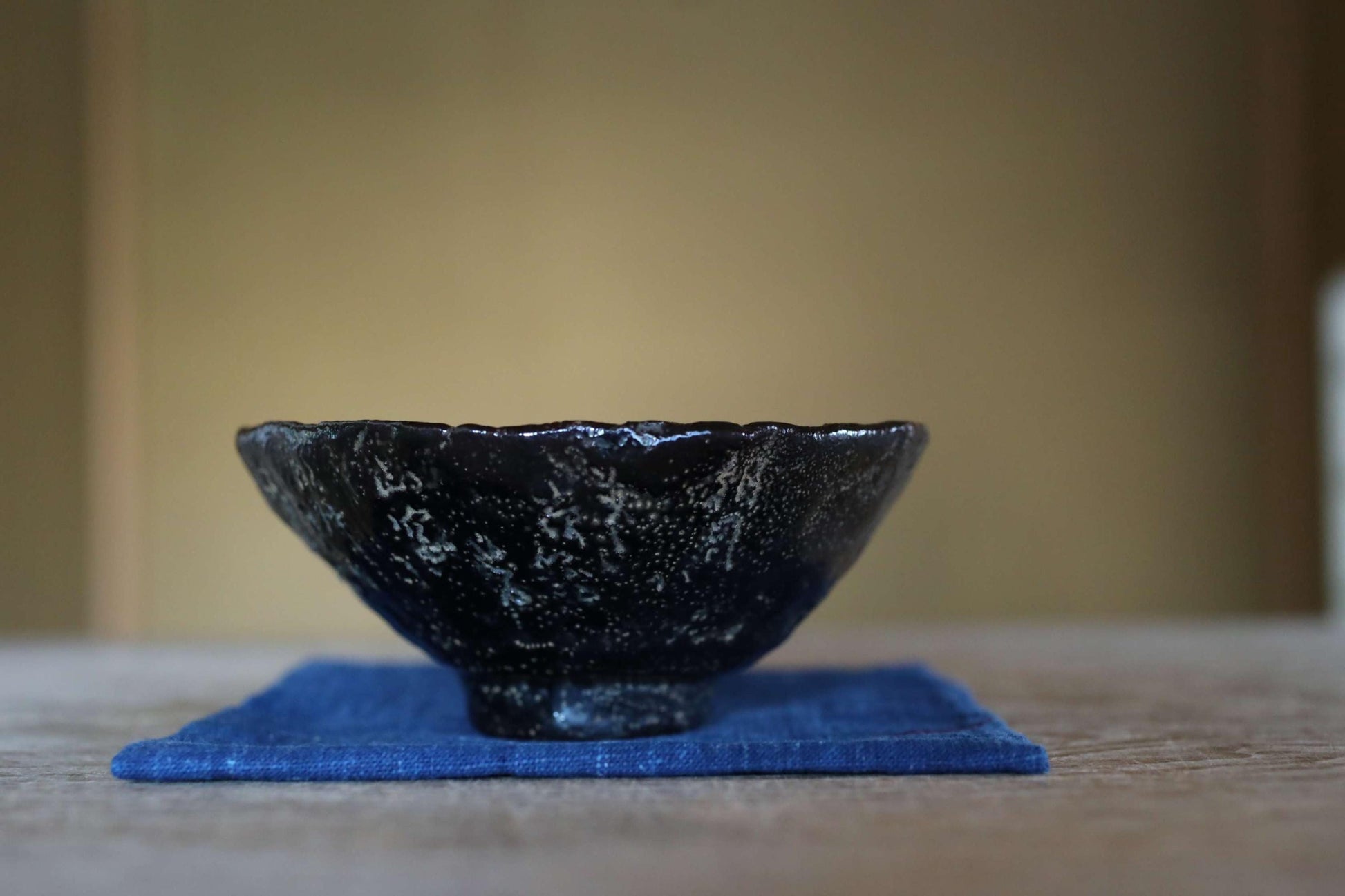 A black ceramic bowl with a textured surface sits on a blue cloth on a wooden surface.