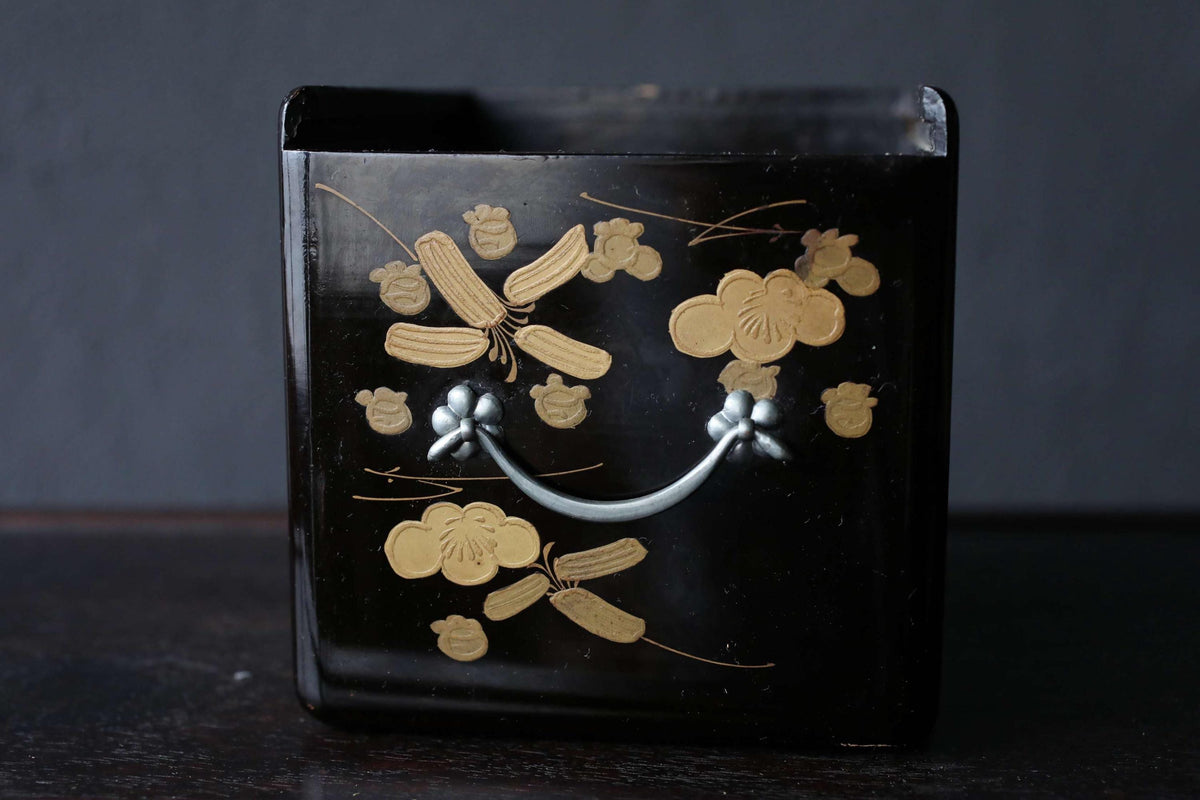 A black container with a handle and gold floral designs on it.