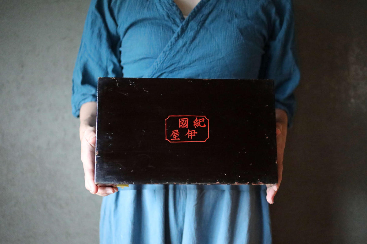 A person wearing a blue shirt is holding a black rectangular object with red text on it.