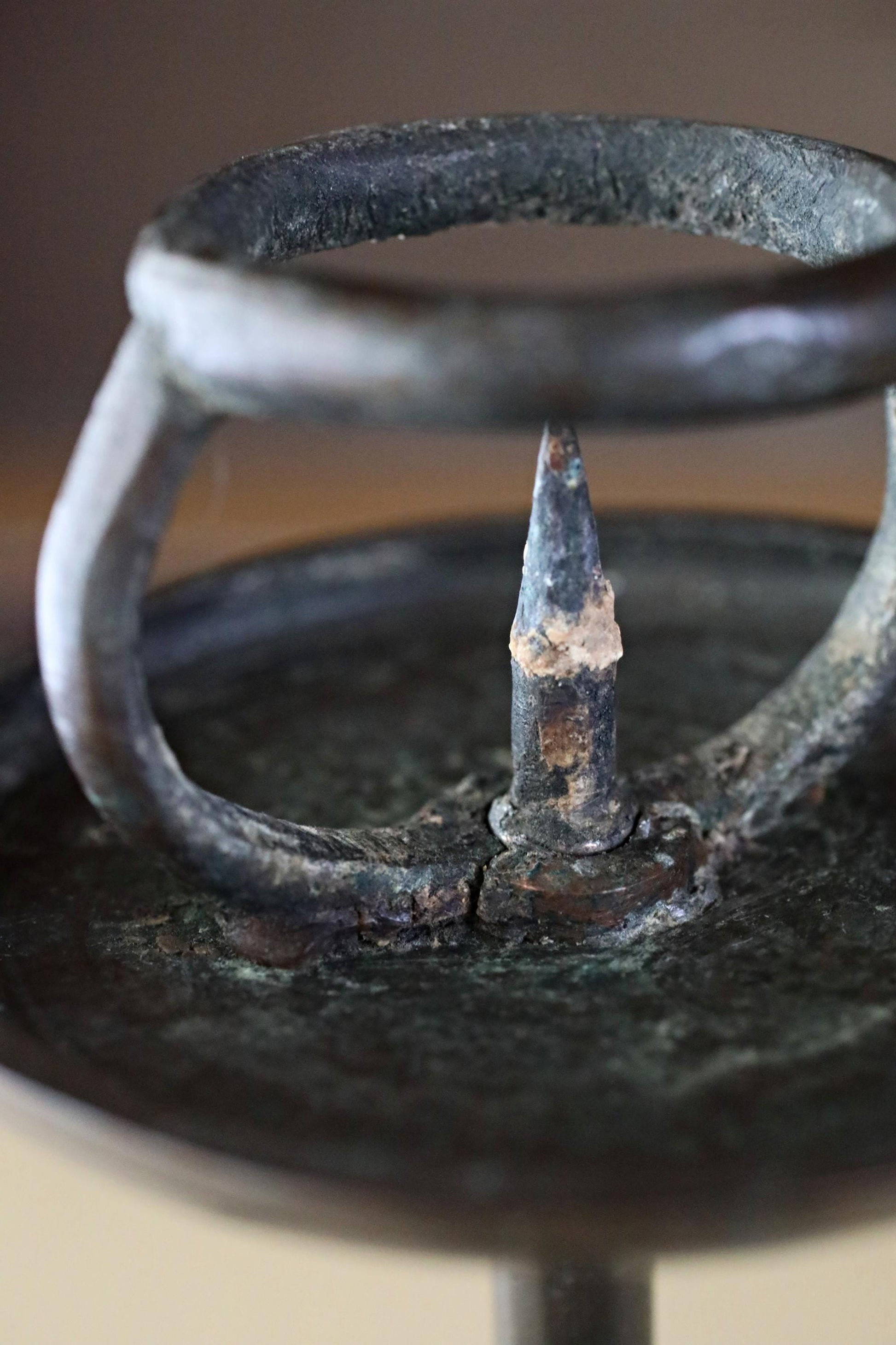 A close-up view of a rusted metal object, possibly a candle holder or a piece of machinery, with a sharp, pointed end and a worn, weathered appearance.