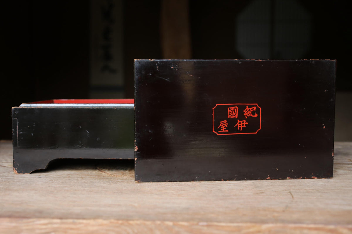 A black rectangular box with a red Chinese character on it, placed on a wooden surface.