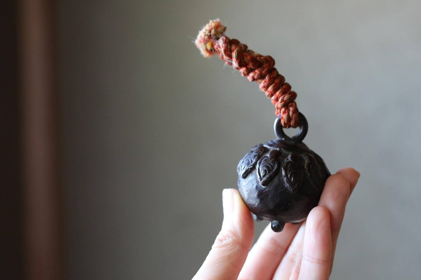 A hand holding a small, round, black object with a red string or cord attached to it.