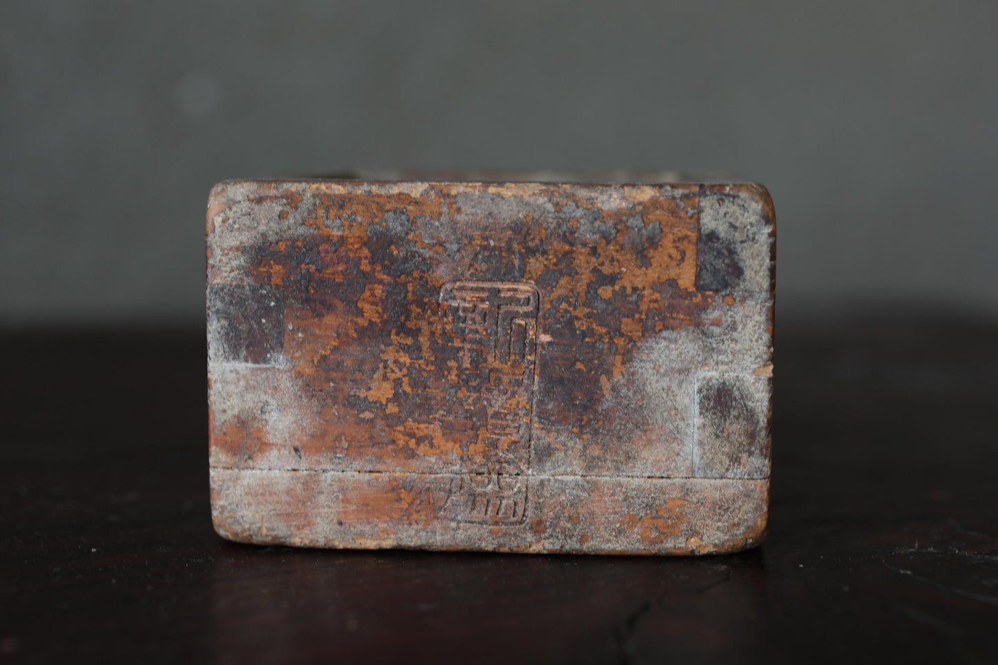 a weathered, rusted metal object with a Chinese character etched into it, sitting on a dark surface.