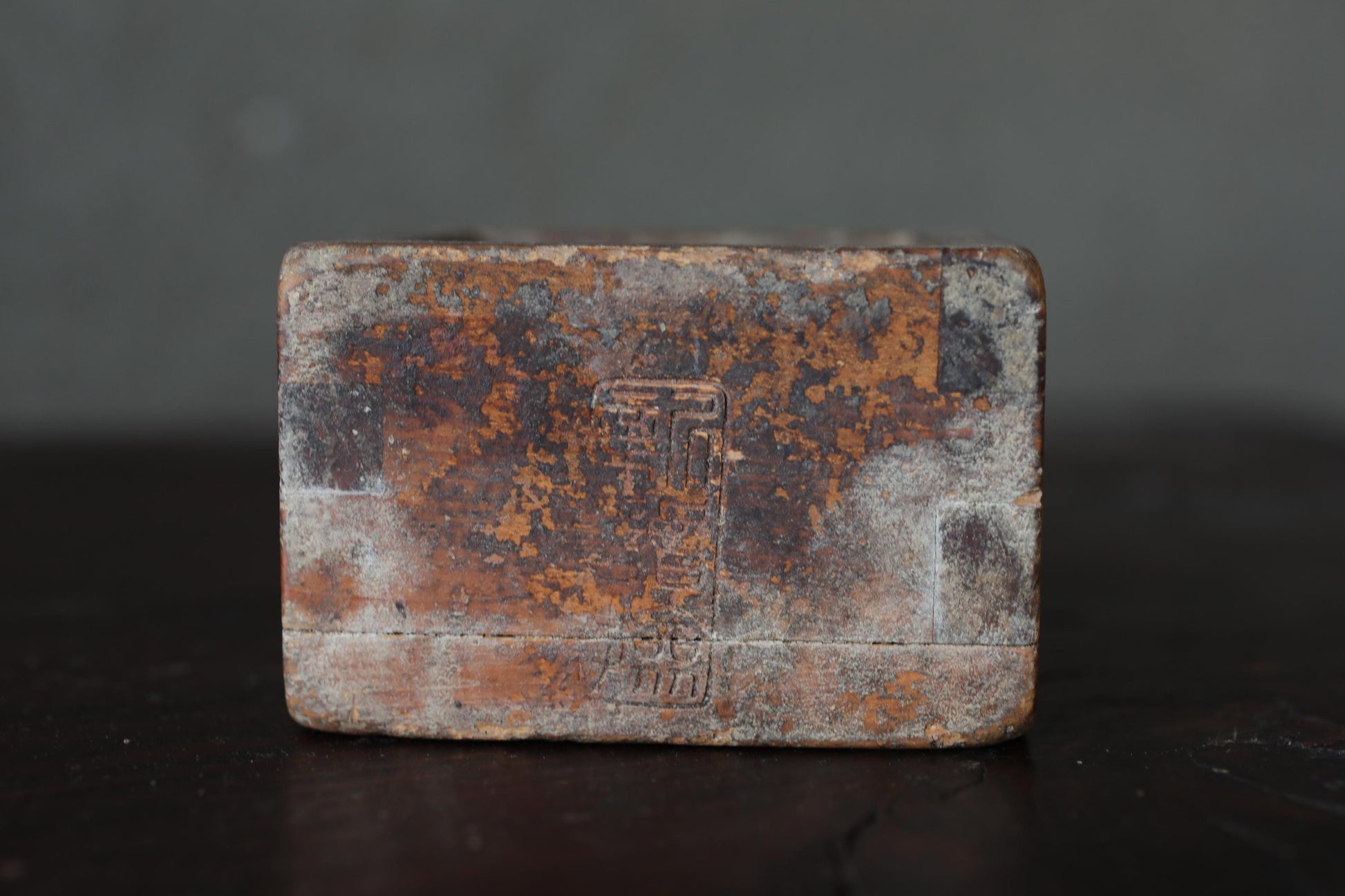 a weathered, rusted metal object with a Chinese character etched into it, sitting on a dark surface.