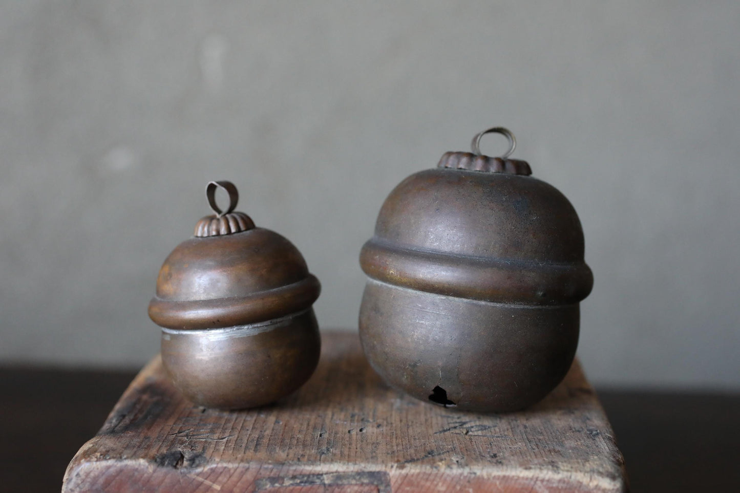 Two antique brass bells with round domes sit on a wooden surface against a plain background.