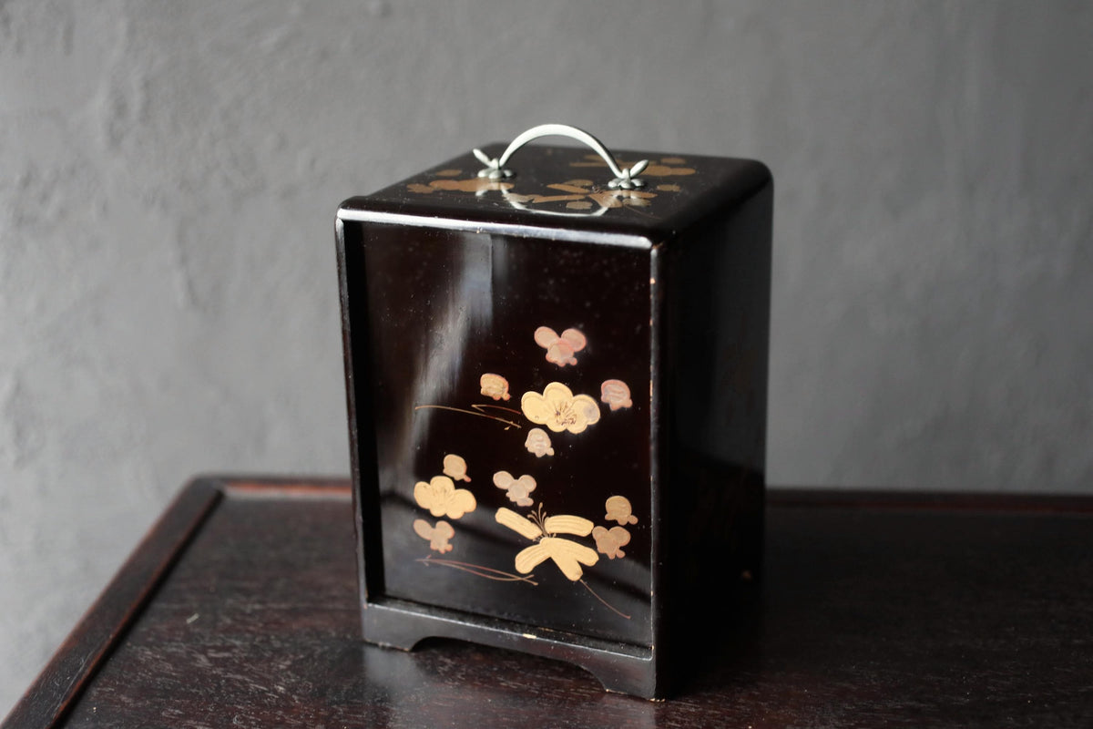 A black wooden box with a floral design on it, sitting on a dark surface.
