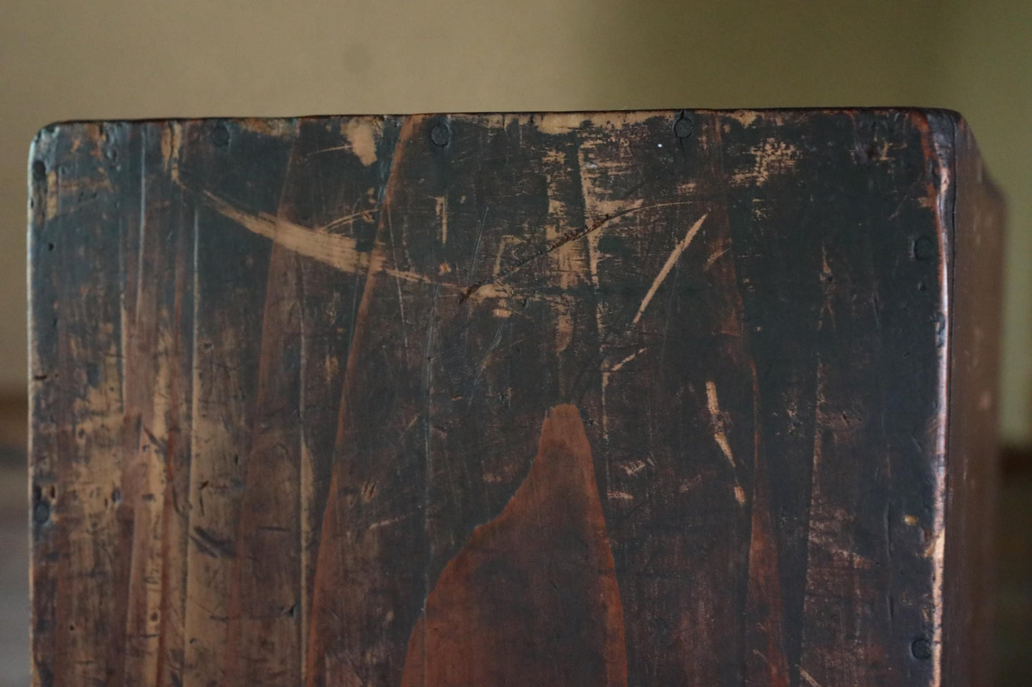 a close-up view of a weathered, dark wooden surface with visible scratches and marks, suggesting it has been exposed to the elements for an extended period of time.