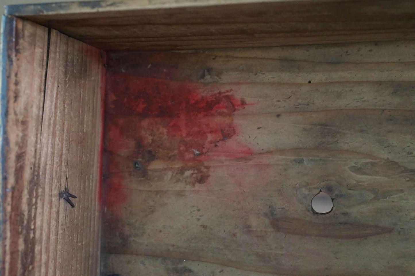 a close-up view of a wooden surface with a red stain on it, and a small hole in the wood.