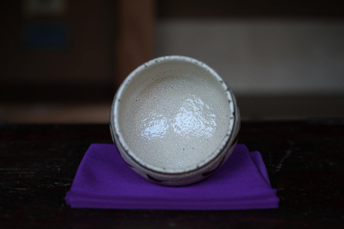 A white ceramic bowl with a textured surface sits on a purple cloth on a dark surface.