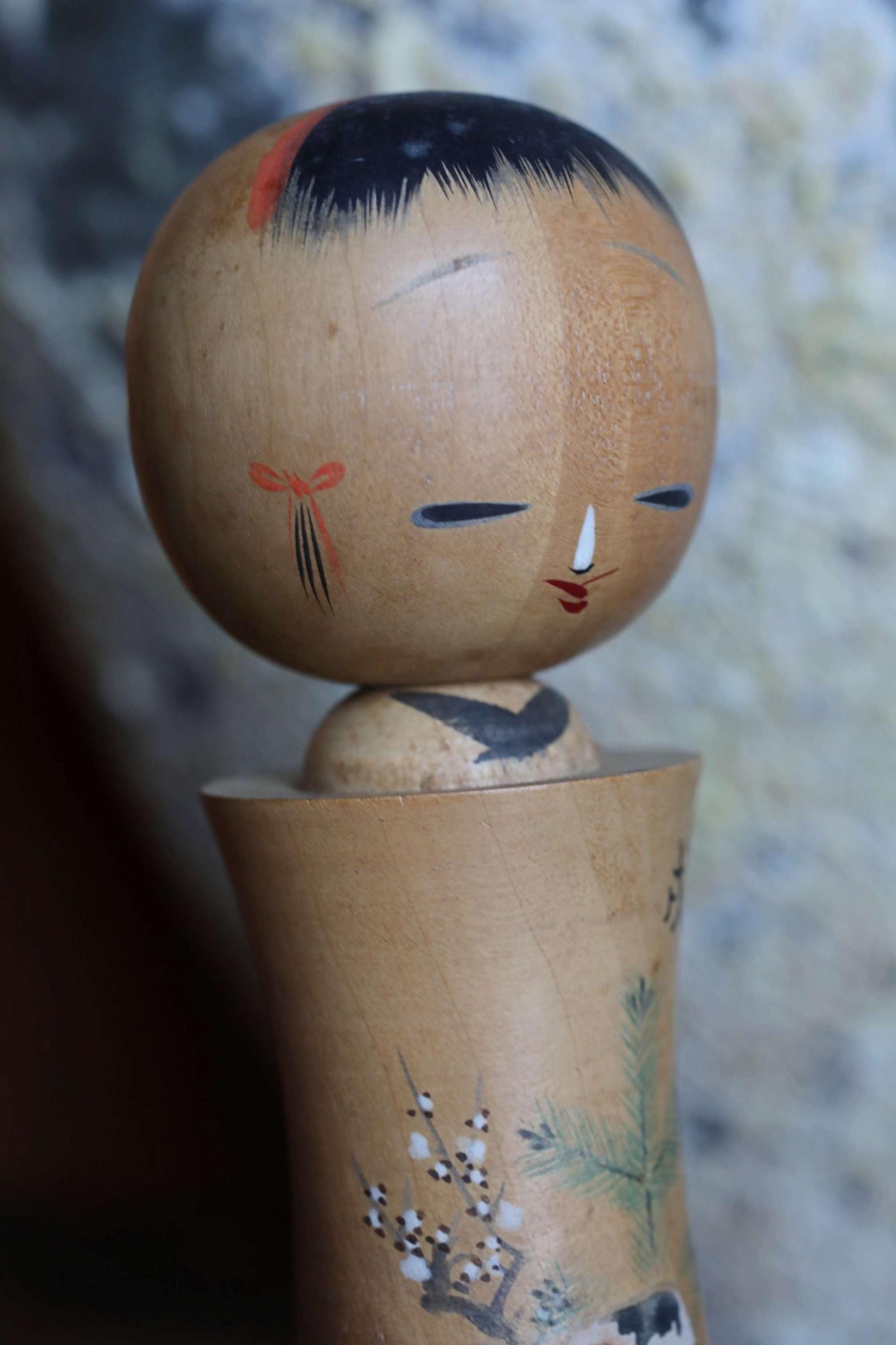 A wooden doll with a face and a bow on its head, sitting on a wooden base with a floral design.