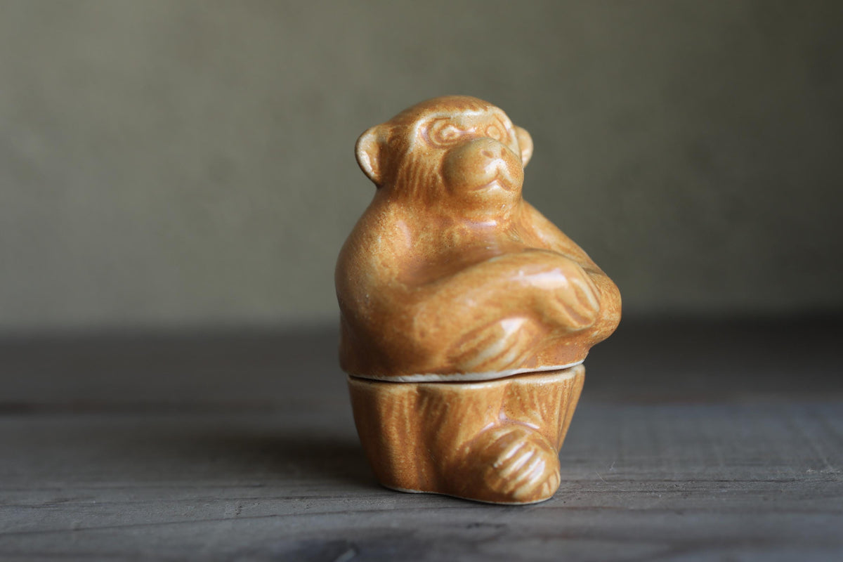 A ceramic figurine of a monkey sitting on a wooden surface.