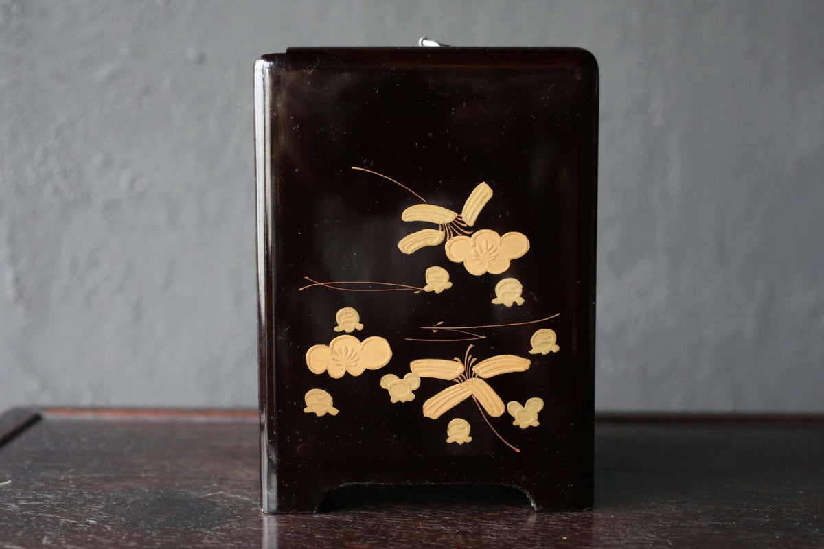 A black rectangular box with a gold floral design on it, sitting on a dark surface.