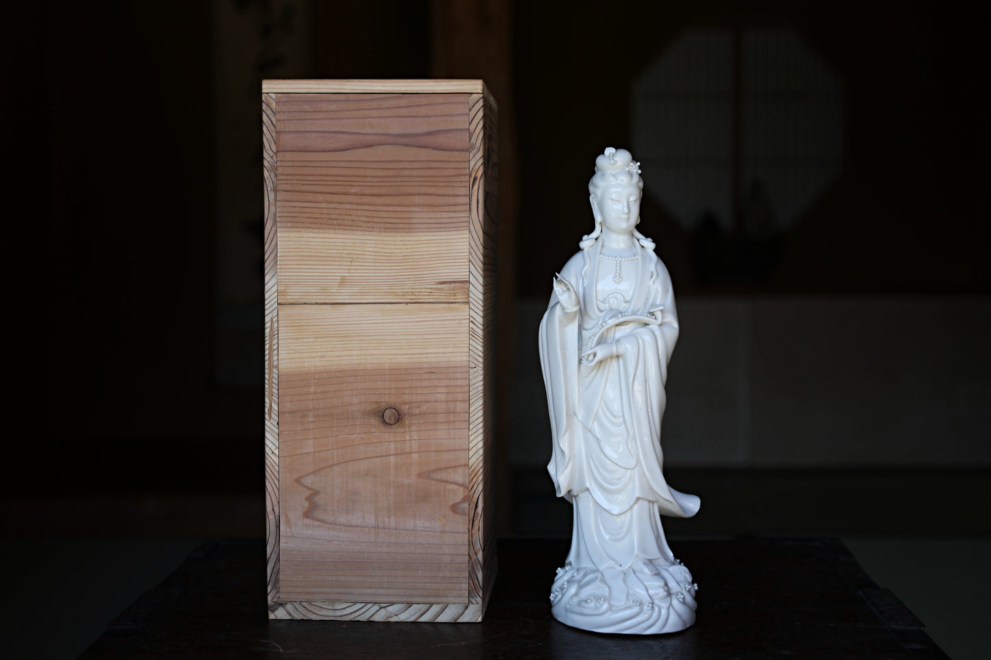 a white ceramic statue of a deity, standing next to a wooden box.