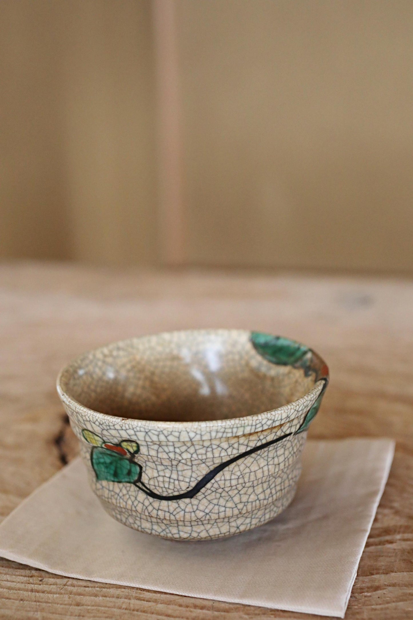 A ceramic bowl with a floral design sits on a beige napkin on a wooden table.